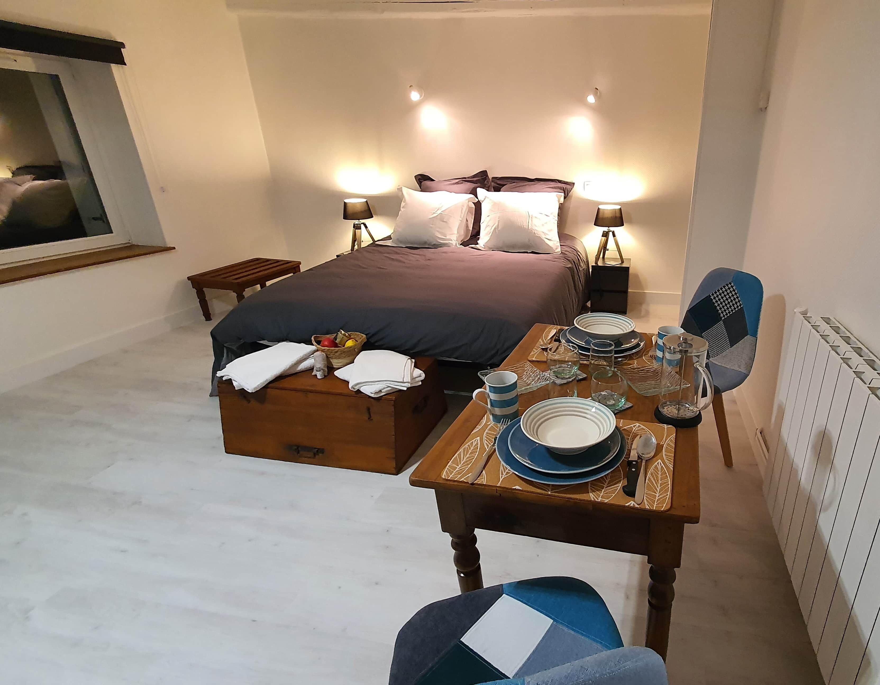 Une chambre bien rangée, avec un lit, des tables de chevet, une lampe de chevet, une table préparée pour le petit-déjeuner et une chaise.