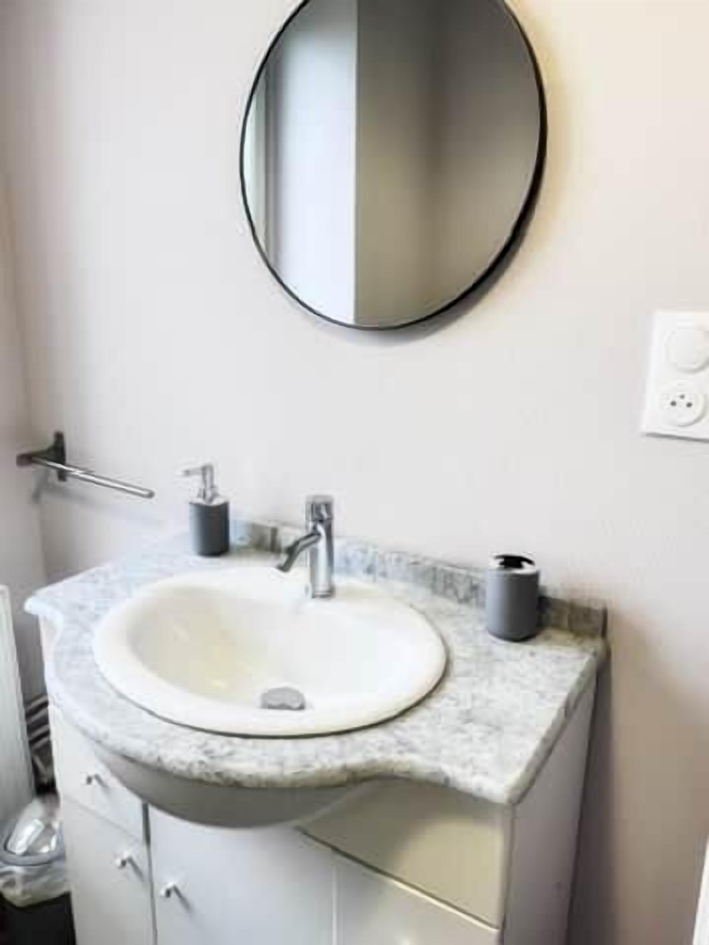 Un bagno con uno specchio rotondo, un lavandino bianco e un ripiano in marmo.