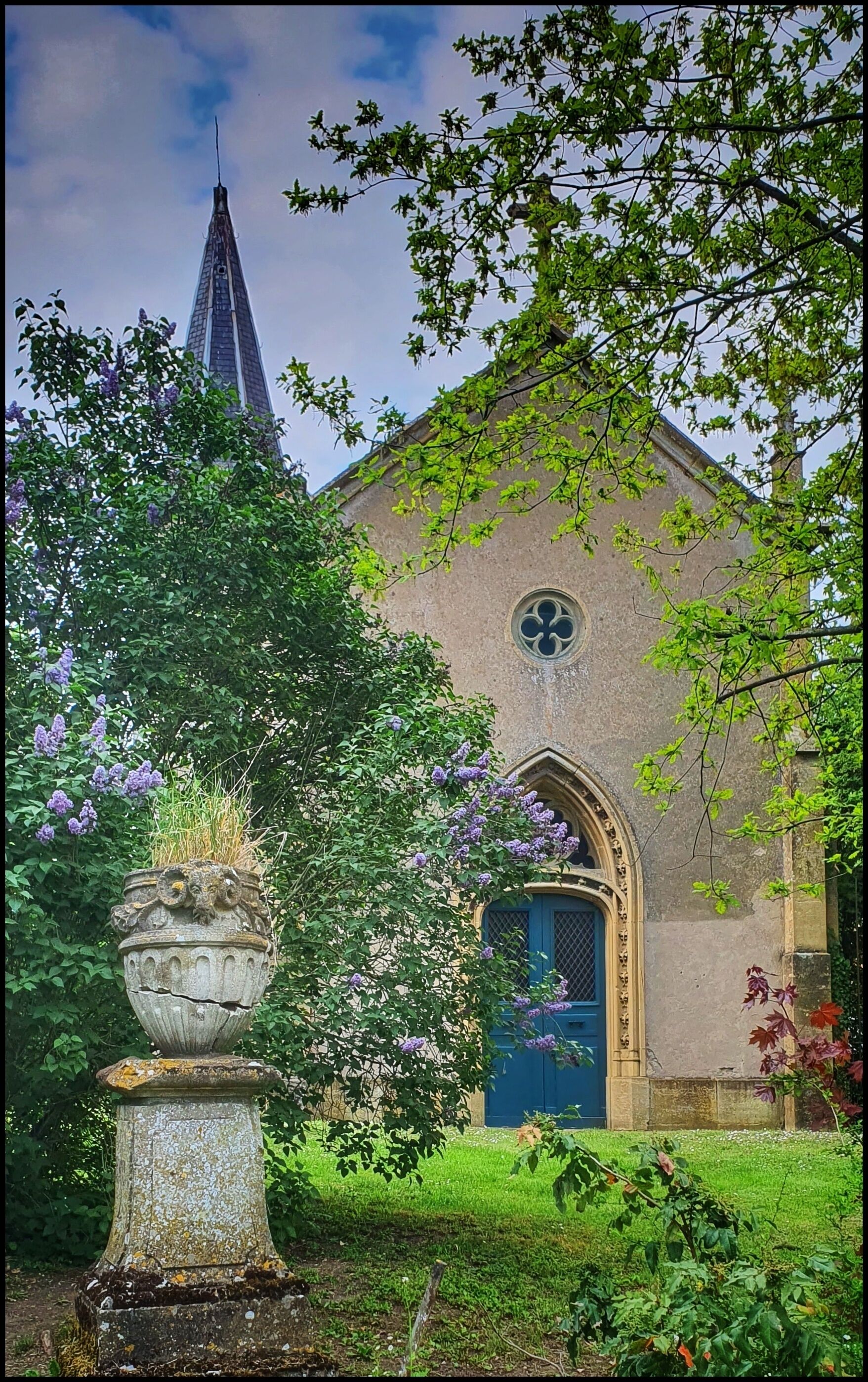 A church with a blue door, surrounded by greenery and a large stone urn.