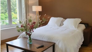 A hotel room with a large bed, two bedside lamps, a vase with flowers on a nightstand, and a window with a view of greenery. - Appart 4, rustique (Rurange-lès-Thionville)
