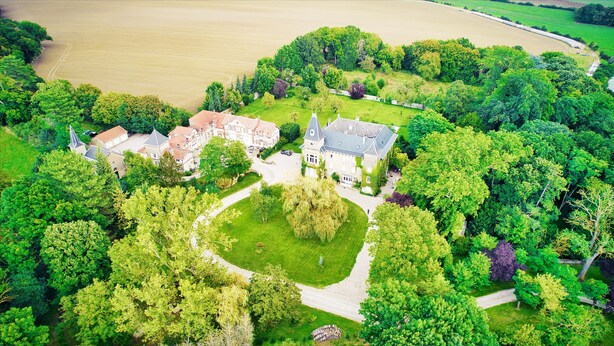 An aerial view of a large estate with multiple buildings, a well-maintained lawn, and a surrounding forest. - Appart 4, rustique (Rurange-lès-Thionville)
