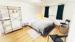 Ein Schlafzimmer mit Bett, Kleiderschrank, Stuhl, einem Fenster mit Vorhängen und einem kleinen Tisch.