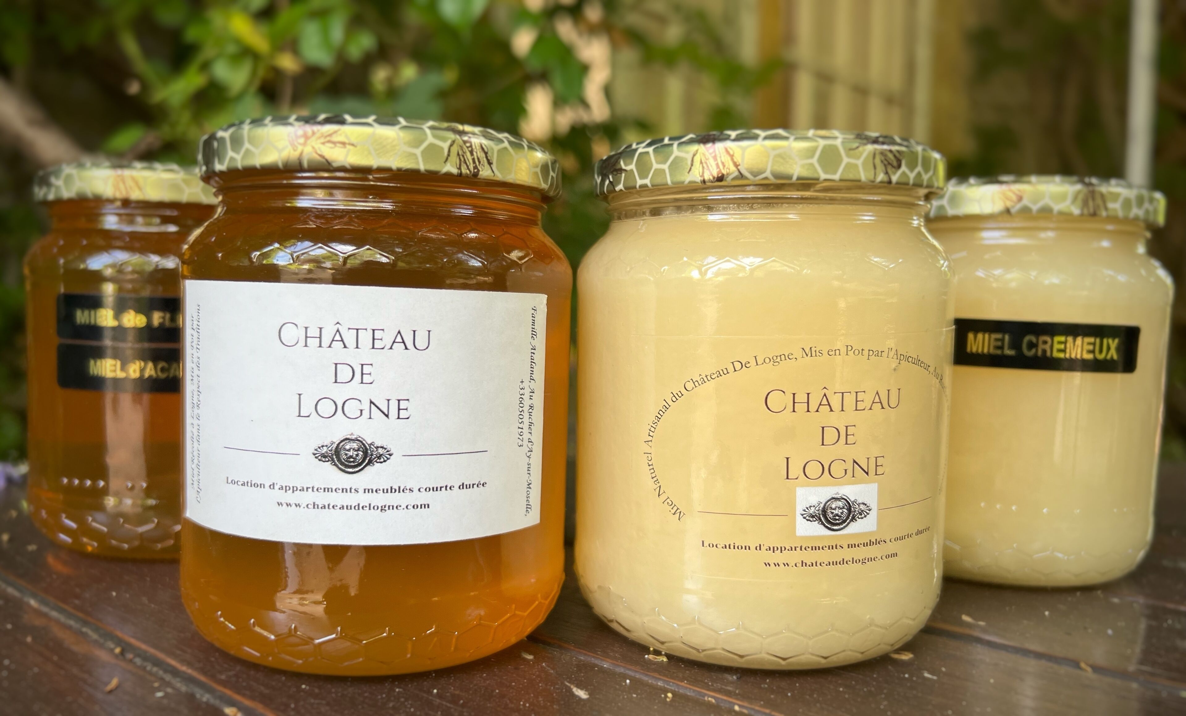 Four jars of honey and cream with labels, placed on a wooden surface.