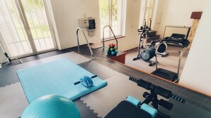 Ein Heimfitnessstudio mit Trainingsgeräten, darunter ein Laufband, ein Ergometer und Gewichte.