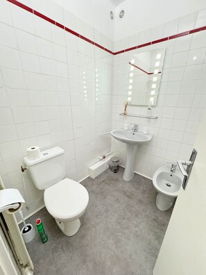 Ein modernes Badezimmer mit weißen Fliesen, Toilette, Bidet, Waschbecken und Spiegel.