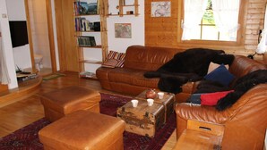 Ein gemütliches Wohnzimmer mit einem braunen Ledersofa, dazu passendem Hocker und einem alten Koffer. Ein schwarzer Hund ruht sich auf dem Sofa aus.