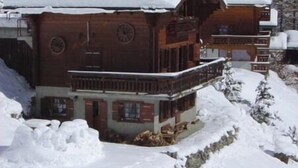 Eine Holzchalet mit Balkon, umgeben von schneebedeckten Bergen.