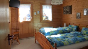 Ein Schlafzimmer mit Holzwandverkleidung, zwei Betten, einem Fernseher und einem kleinen Hocker.