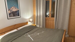 Een slaapkamer met een houten bed, een nachtkastje, een lamp, een raam met gordijnen, en een poster aan de muur.