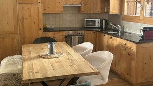Een keuken met houten kastjes, een magnetron, een fornuis en een eettafel met stoelen.
