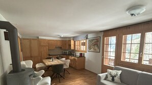 Een gezellige woonkamer met een open haard, een bank, een eethoek en een keuken met houten kastjes.