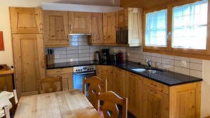 Una cocina con gabinetes de madera, encimera negra, estufa y ventana con persianas.