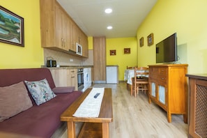 Un espacio habitable compacto con sofá, una mesa de comedor, una zona de cocina y un televisor.