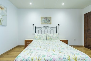 Un dormitorio con colcha estampada, cabecero de metal, mesitas de noche y puerta de madera.