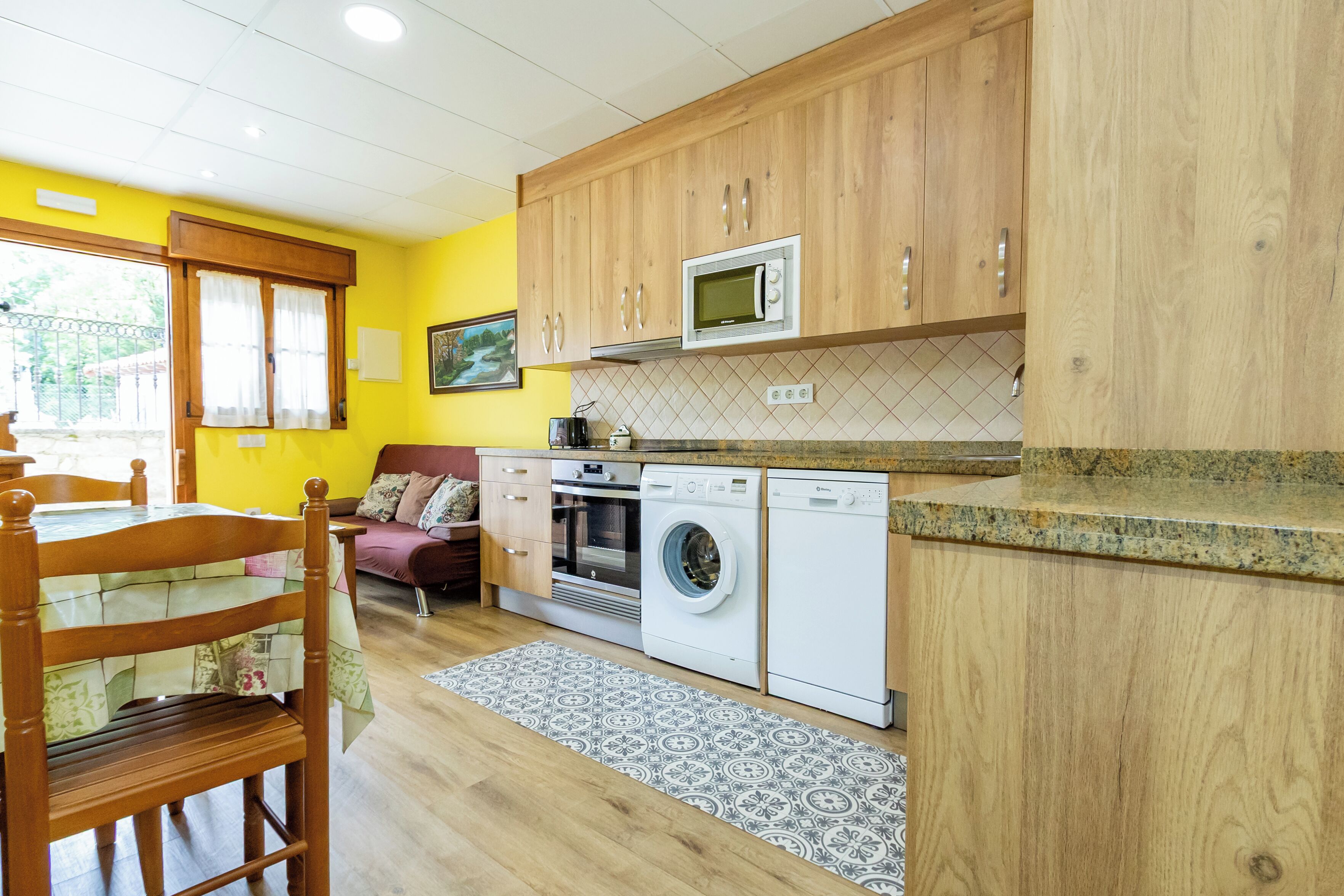 Une cuisine compacte dotée de meubles en bois, d’un four à micro-ondes, d’un lave-linge et d’un coin repas avec une table et des chaises.