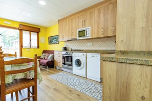 A compact kitchen with wooden cabinets, a microwave, a washing machine, and a dining area with a table and chairs. - Apartments La Huerta de la Torre ( Apartment number 1 ) (Cangas de Onis)