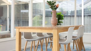 Ein Essbereich mit Holztisch, weißen Stühlen, großen Fenstern und einem blau gemusterten Teppich.