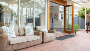 Ein überdachter Patio-Bereich mit Rattanmöbeln und einer Glastür, die zu einem Innenraum führt.