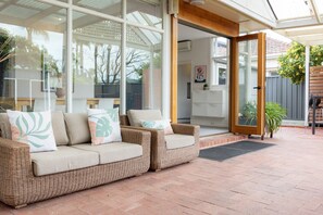 Ein überdachter Patio-Bereich mit Rattanmöbeln und einer Glastür, die zu einem Innenraum führt.