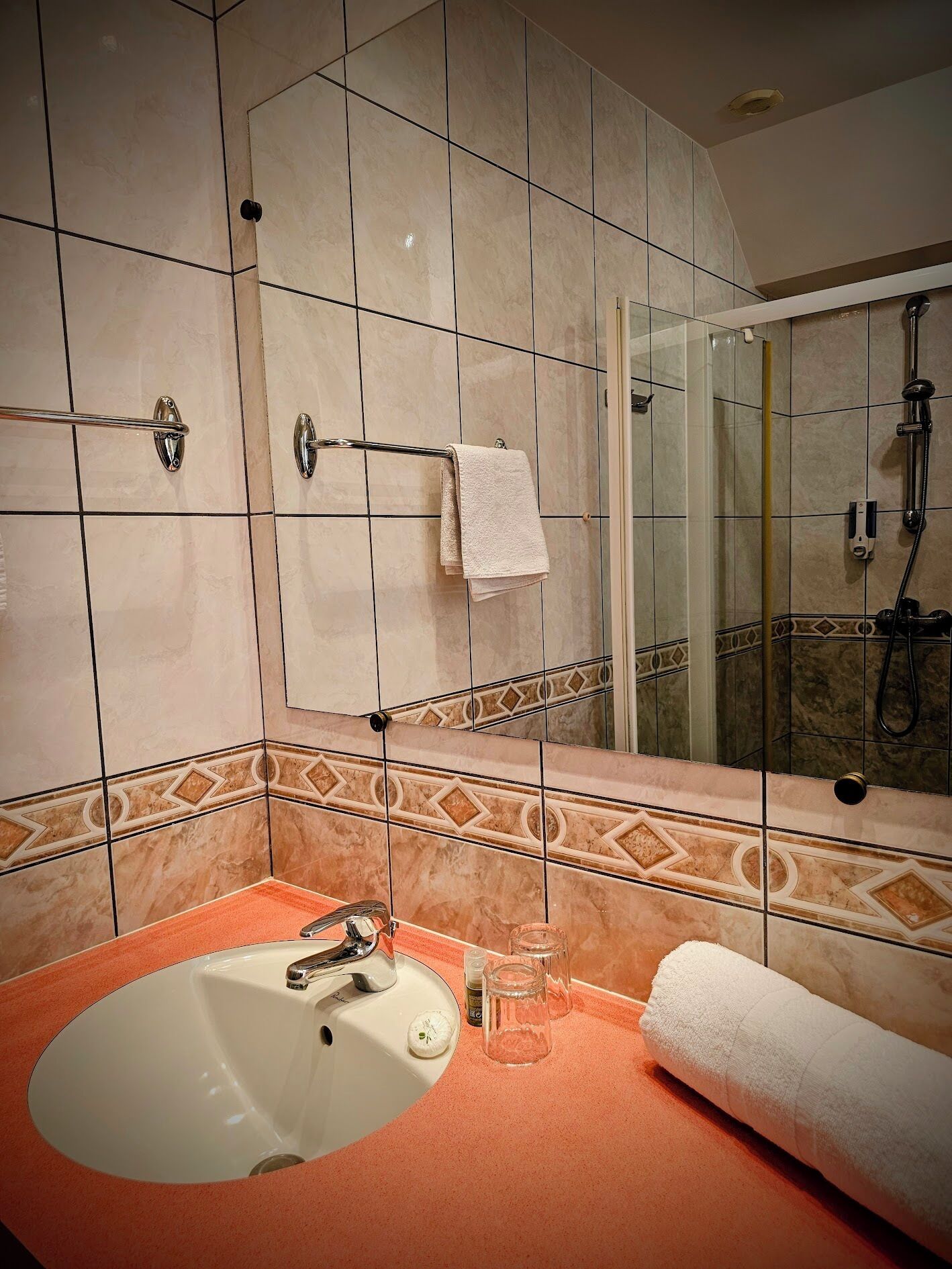 Un baño con un espejo grande, un lavamanos, una ducha y un perchero para toallas.