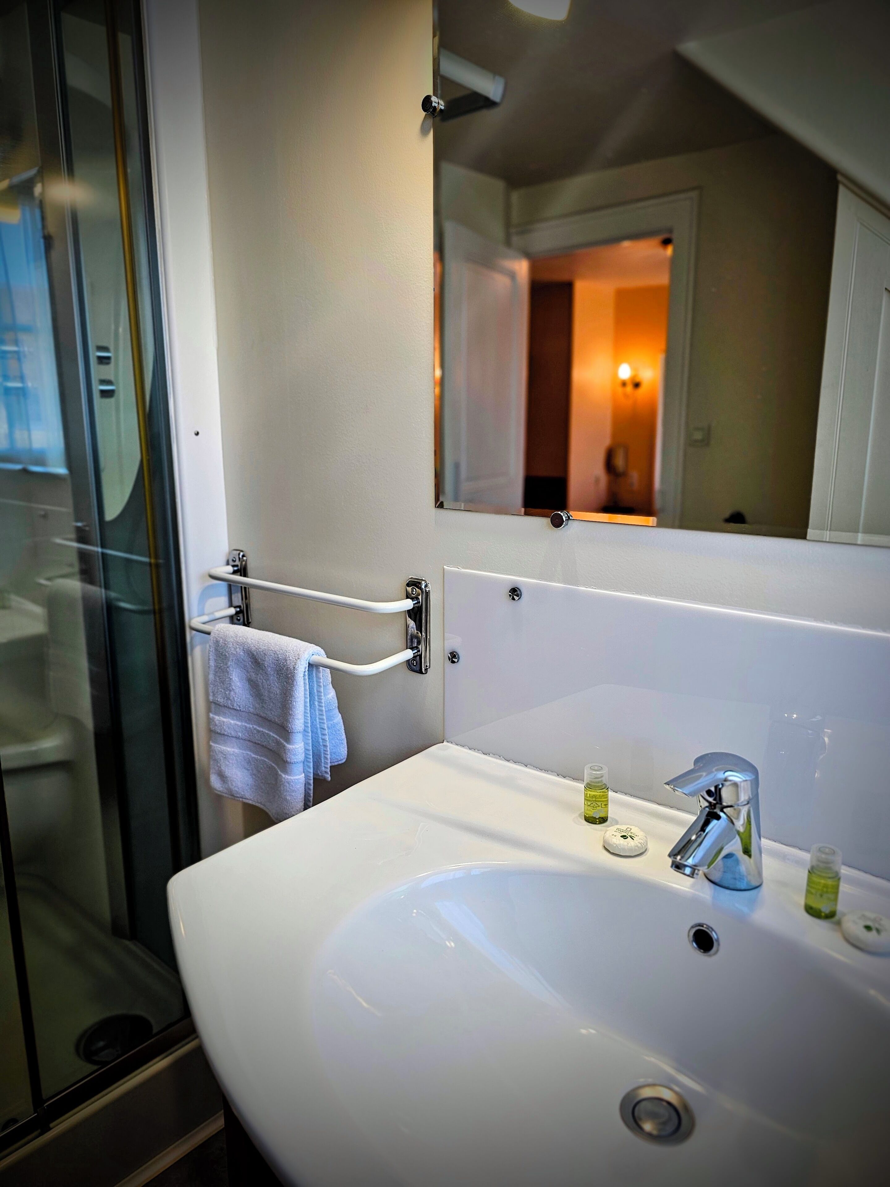 A bathroom with a large white sink, a mirror, and a glass shower enclosure.
