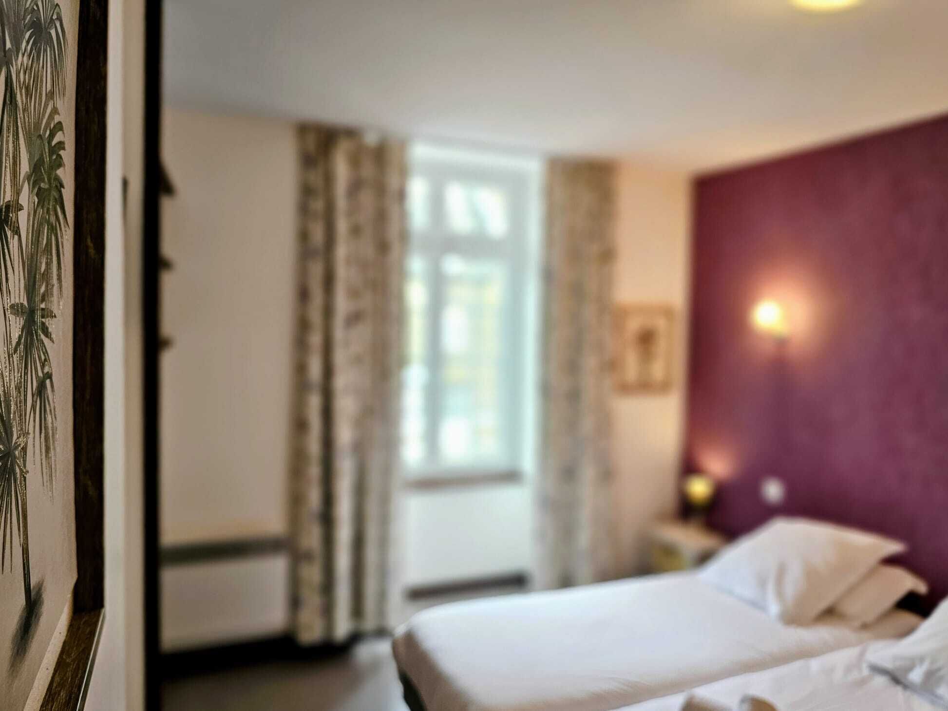 A hotel room with a bed, a nightstand, and a window with curtains.