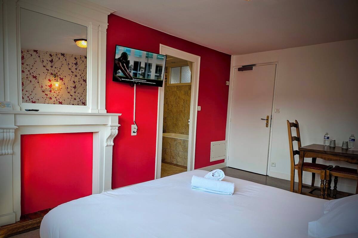 Une chambre d’hôtel avec un lit, un téléviseur fixé au mur, une porte et une petite table sur laquelle se trouvent des bouteilles d’eau.