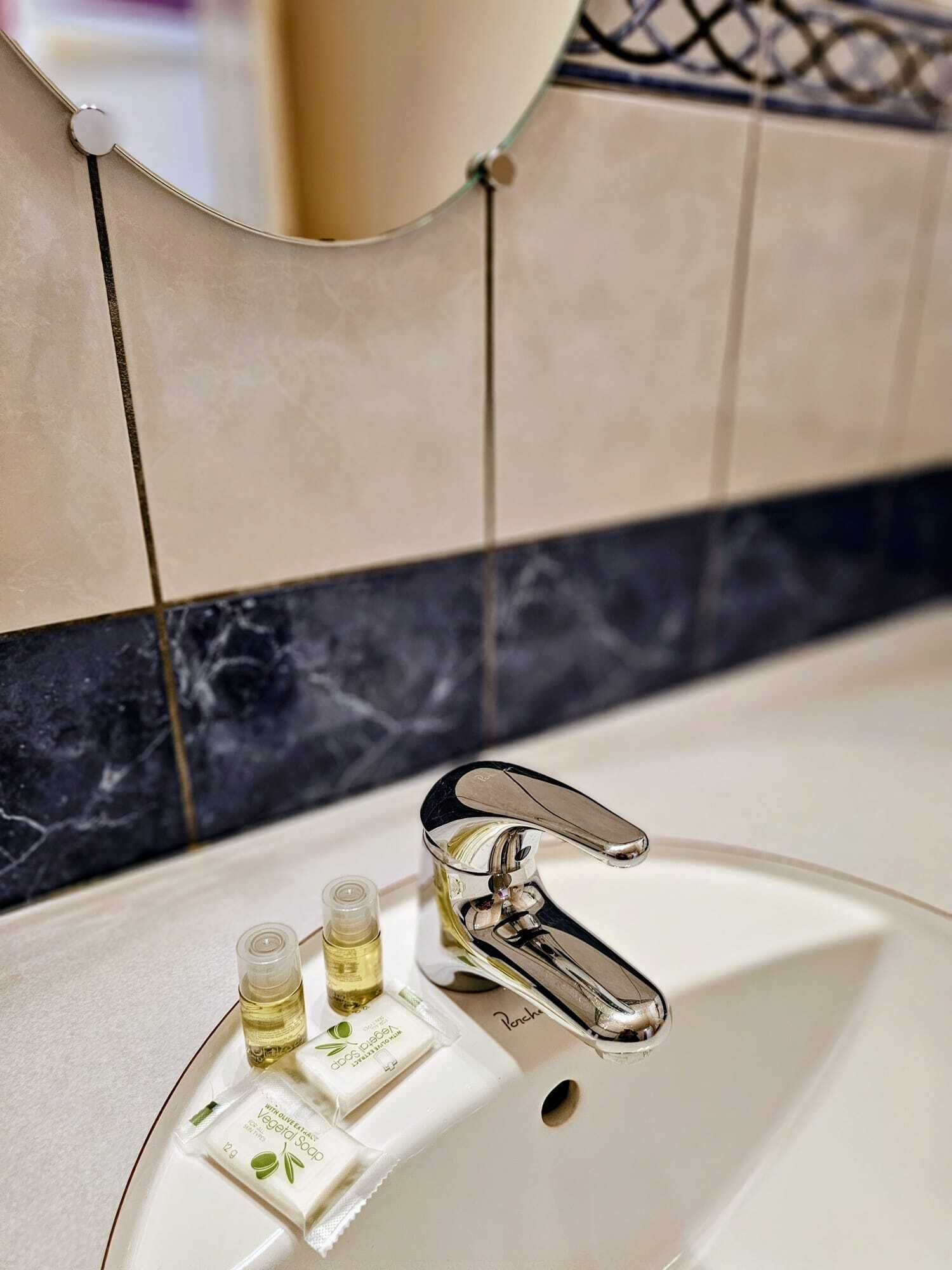 A bathroom sink with a chrome faucet, a mirror above it, and toiletries on the sink.