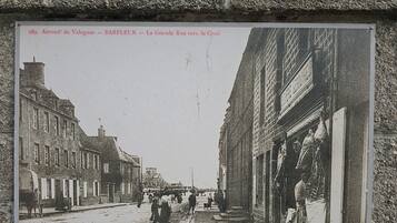 Escena histórica de una calle con edificios, gente y un perro.