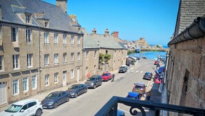 A street view with stone buildings, parked cars, and a clear blue sky. - Le Conquérant (Barfleur)