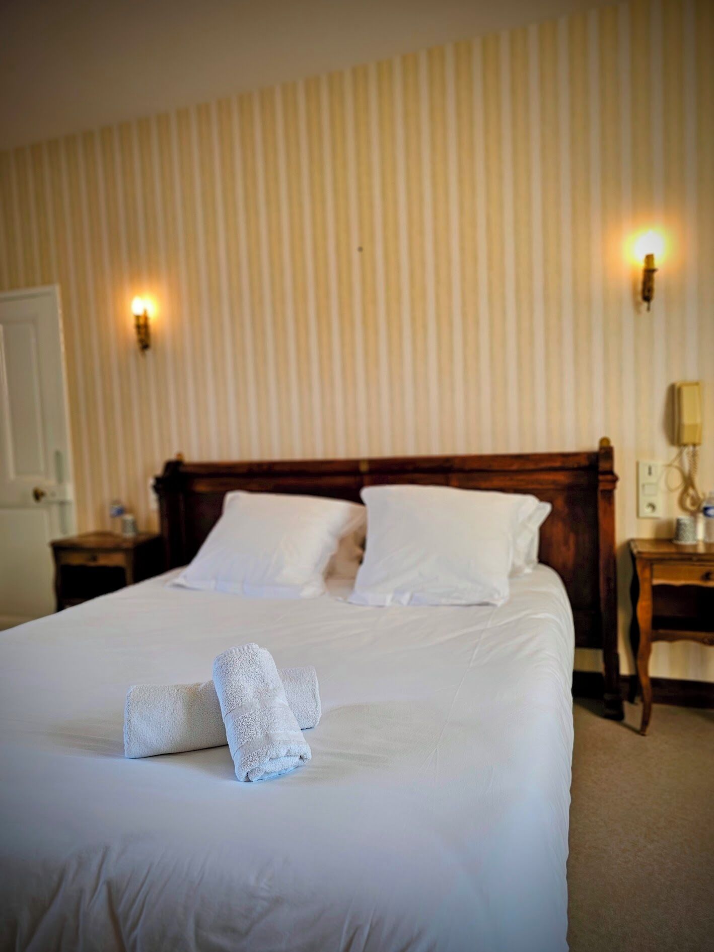 A neatly made bed with white linens and two towels folded at the foot of the bed.