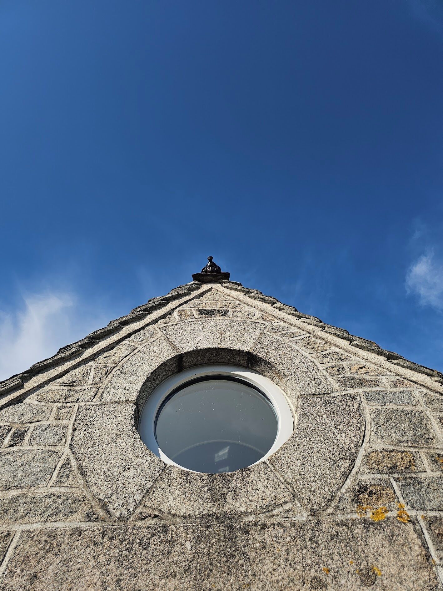 A stone structure with a circular window and a statue on top.