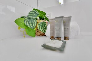 Une salle de bain avec un comptoir blanc, une plante verte et trois produits de soins pour la peau.