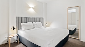 A modern bedroom with a large bed, a bedside table, a lamp, and a mirror. - Modern, Renovated Apartment in Melbourne CBD (Melbourne)