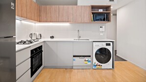 A compact kitchen with a built-in oven, a microwave, a sink, and a washing machine. - Modern, Renovated Apartment in Melbourne CBD (Melbourne)