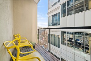 A balcony with yellow chairs and a potted plant, overlooking a modern office building with large windows. - Modern, Renovated Apartment in Melbourne CBD (Melbourne)
