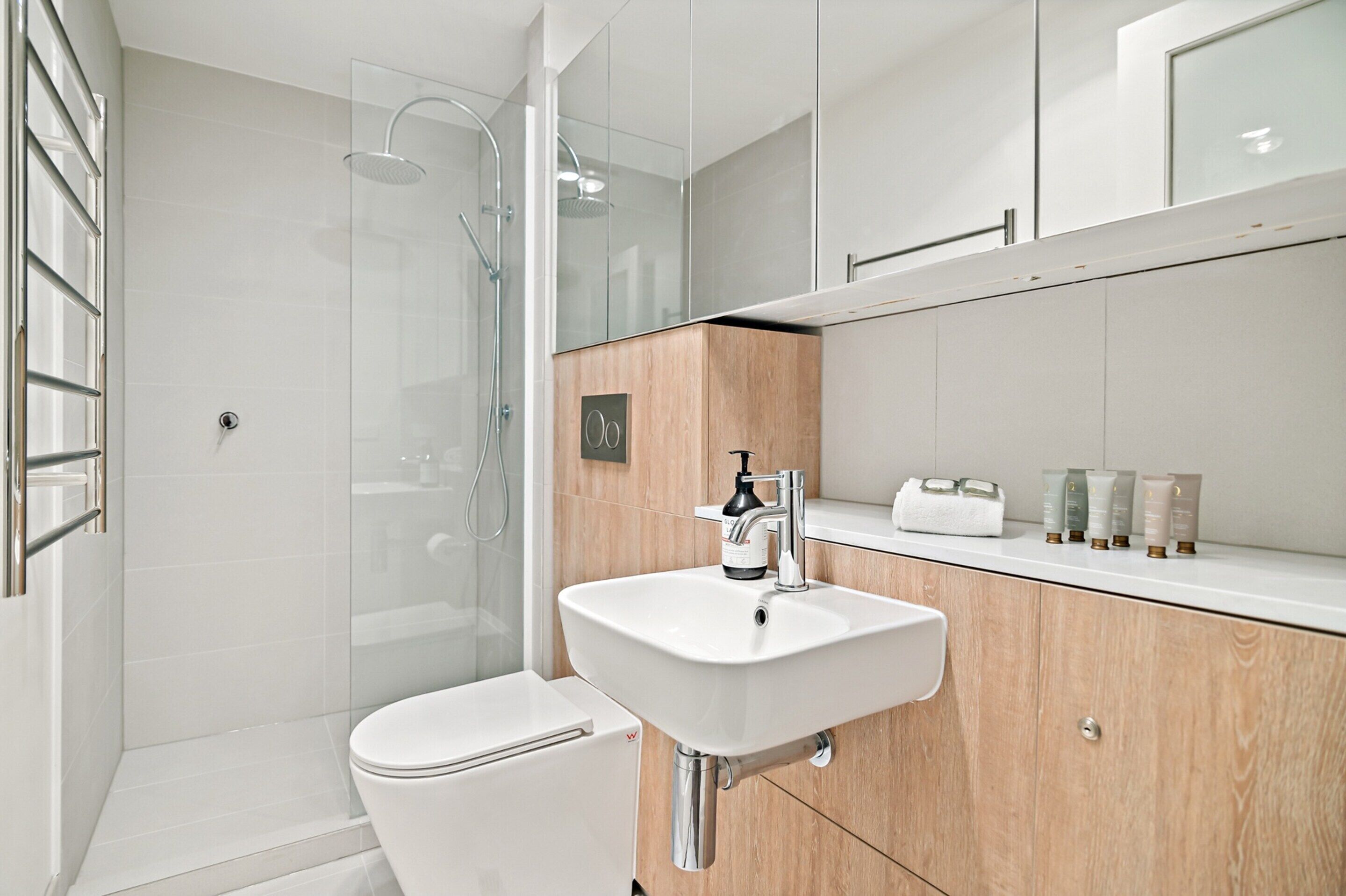 A modern bathroom with a glass-enclosed shower, a white sink, and a wooden vanity.