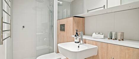 A modern bathroom with a glass-enclosed shower, a white sink, and a wooden vanity.