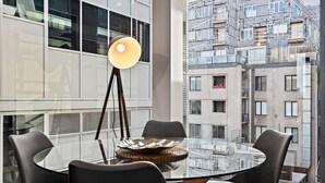 A modern dining area with a glass table, four chairs, and a floor lamp. - Modern, Renovated Apartment in Melbourne CBD (Melbourne)