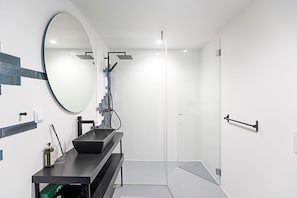 A modern bathroom with a large mirror, a black sink, and a shower area.