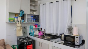 Ett kompakt kök med en gasspis, mikrovågsugn och ett handfat. Det finns hyllor med köksredskap och en hängande påse med texten "MATLAGNING".