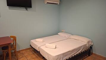 A room with a bed, a TV, an air conditioner, a table, and a chair.