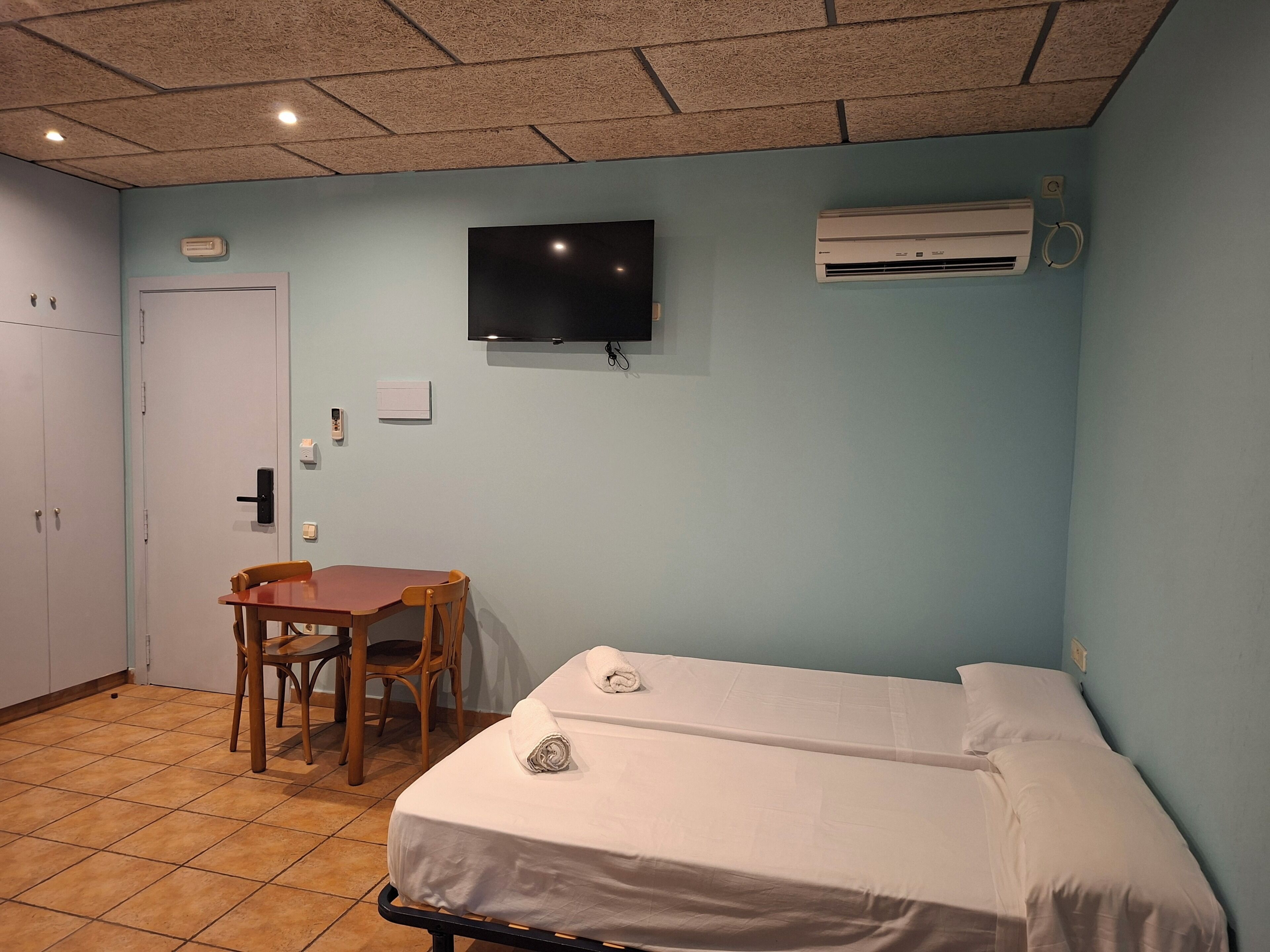 Una habitación con una cama, un escritorio con una silla, un televisor y un aire acondicionado.