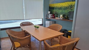 A dining area with wicker chairs, a wooden table, and a view of a field through a window. - Hotel Al Riu  (Bagà)
