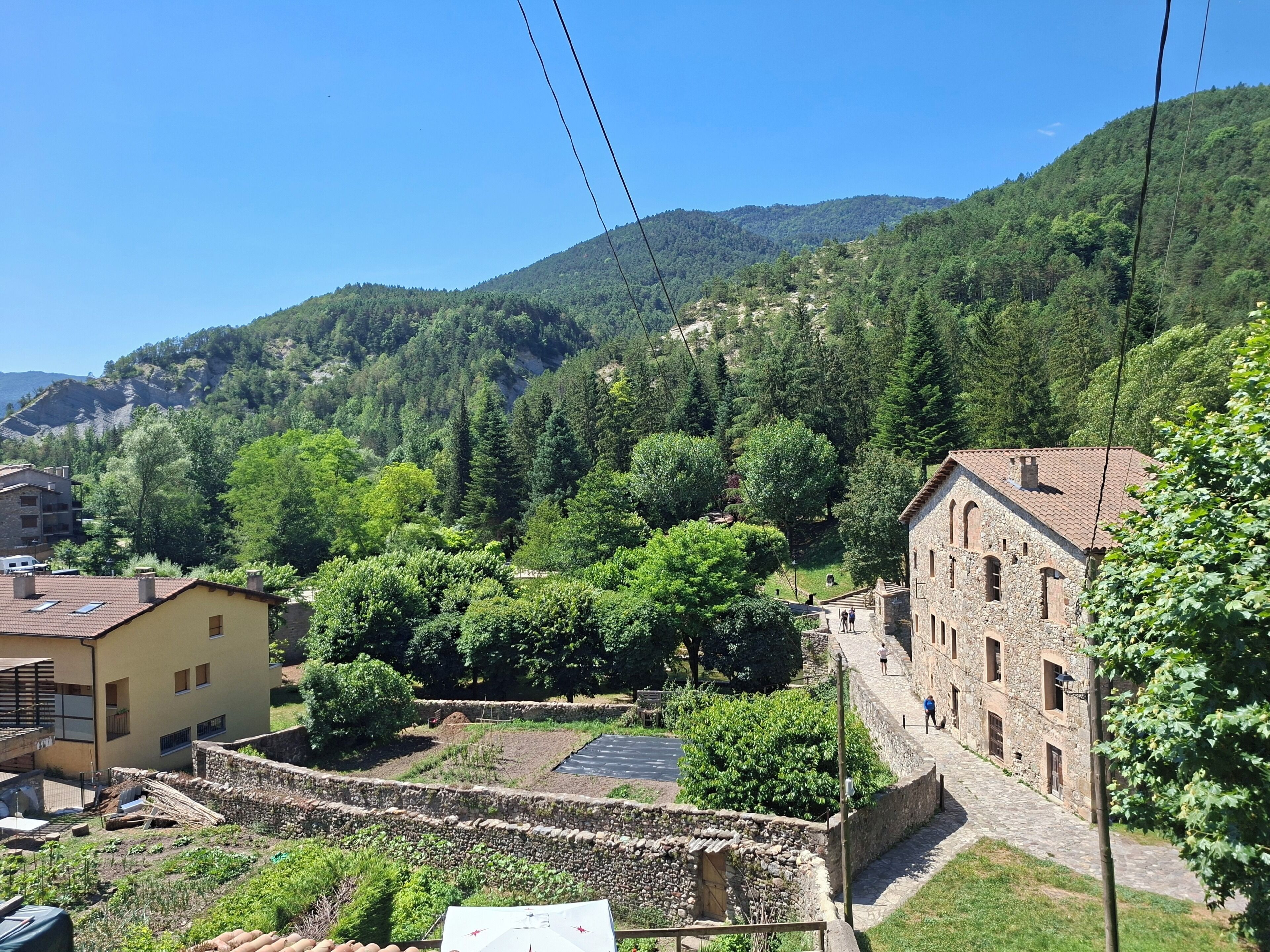 A rural village with stone buildings, a paved area, and lush greenery.