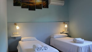 Two single beds with white linens, a wall-mounted air conditioner, and a nightstand with a lamp. - Hotel Al Riu  (Bagà)