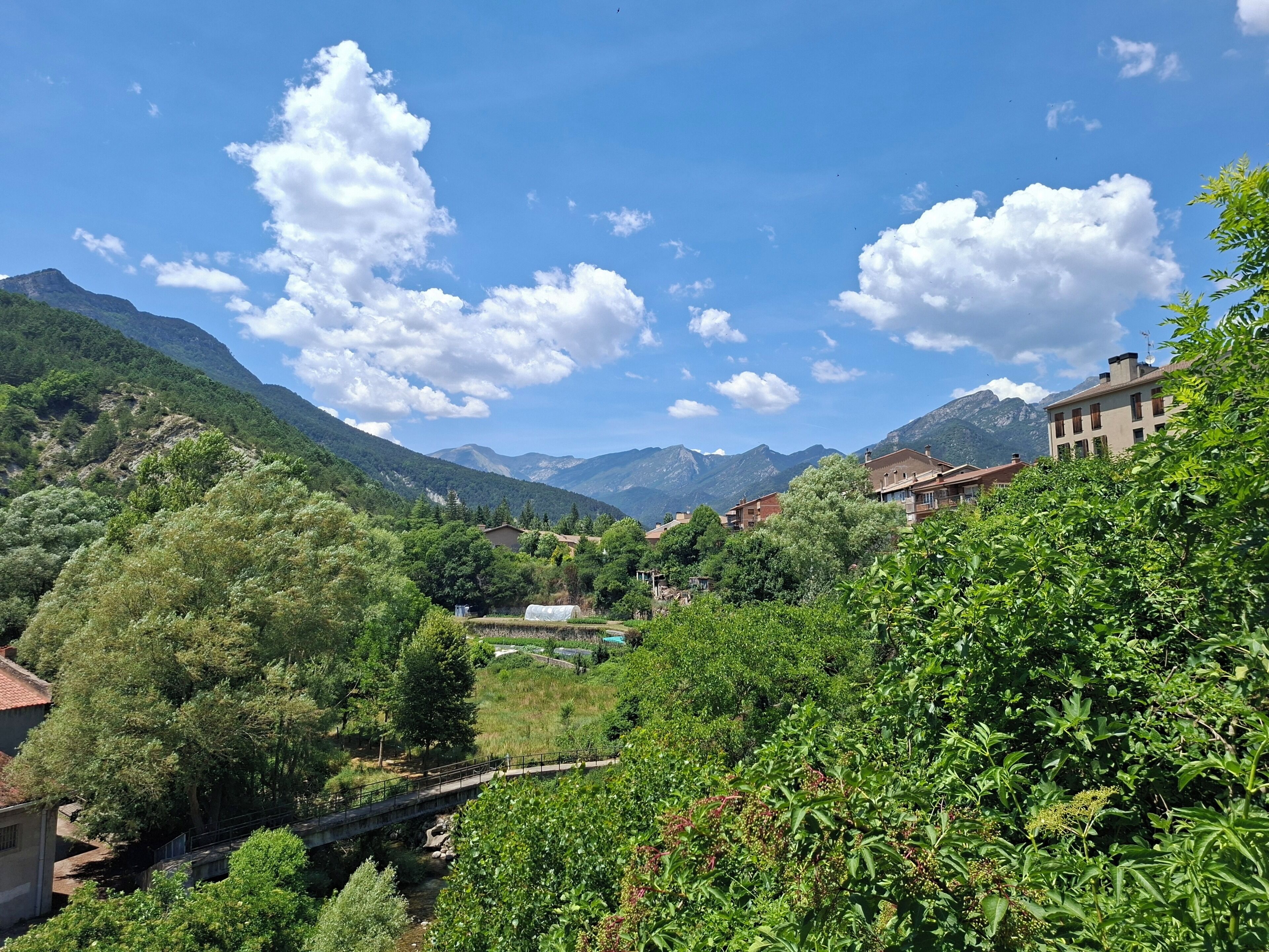 Paisatge de muntanyes amb un riu, un pont i edificis d'arquitectura tradicional.