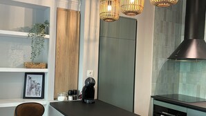 Eine moderne Küche mit einer zentralen Kochinsel, Barhocker, Pendelleuchten, einer Kaffeemaschine und einer Edelstahl-Dunstabzugshaube.