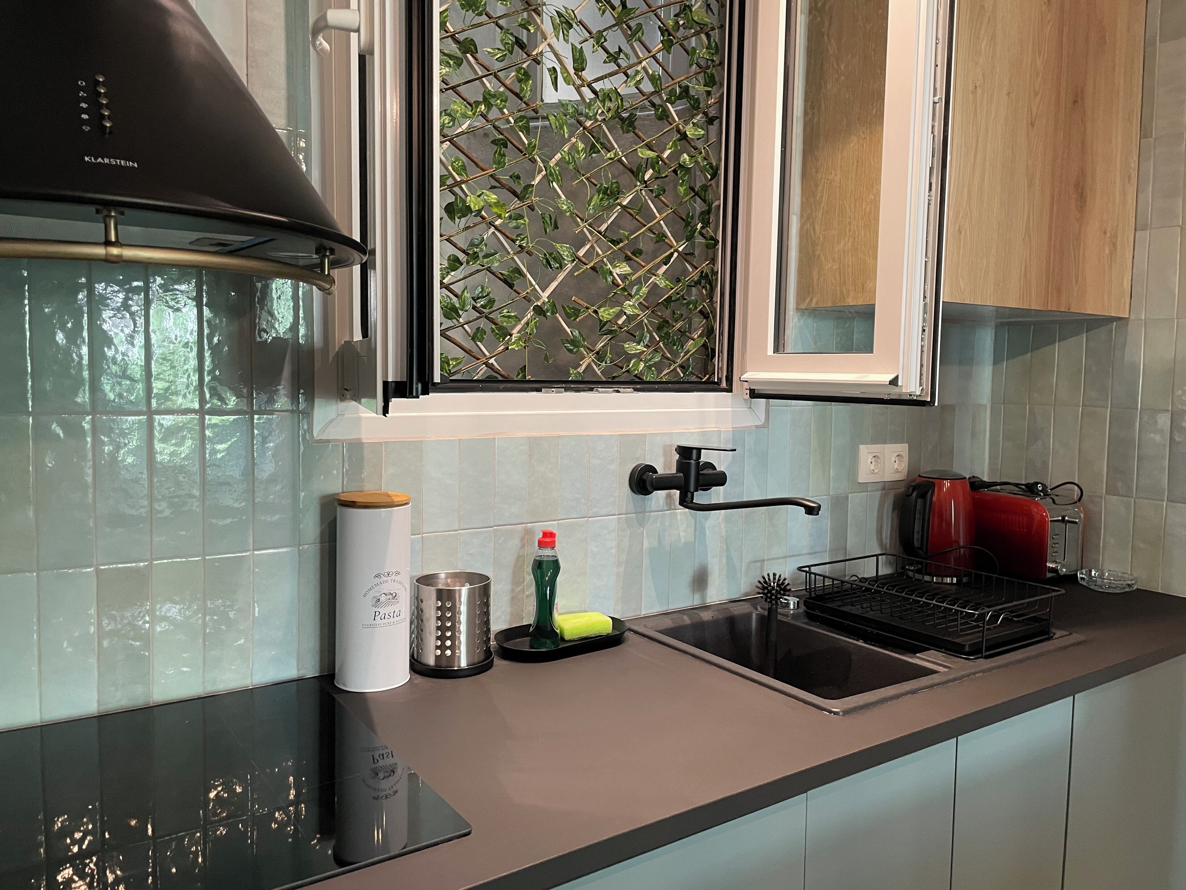 Une cuisine moderne avec un four encastré, une fenêtre agrémentée d’une plante et un grille-pain rouge.