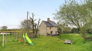 A stone house with a grassy yard, a swing set, and a slide.